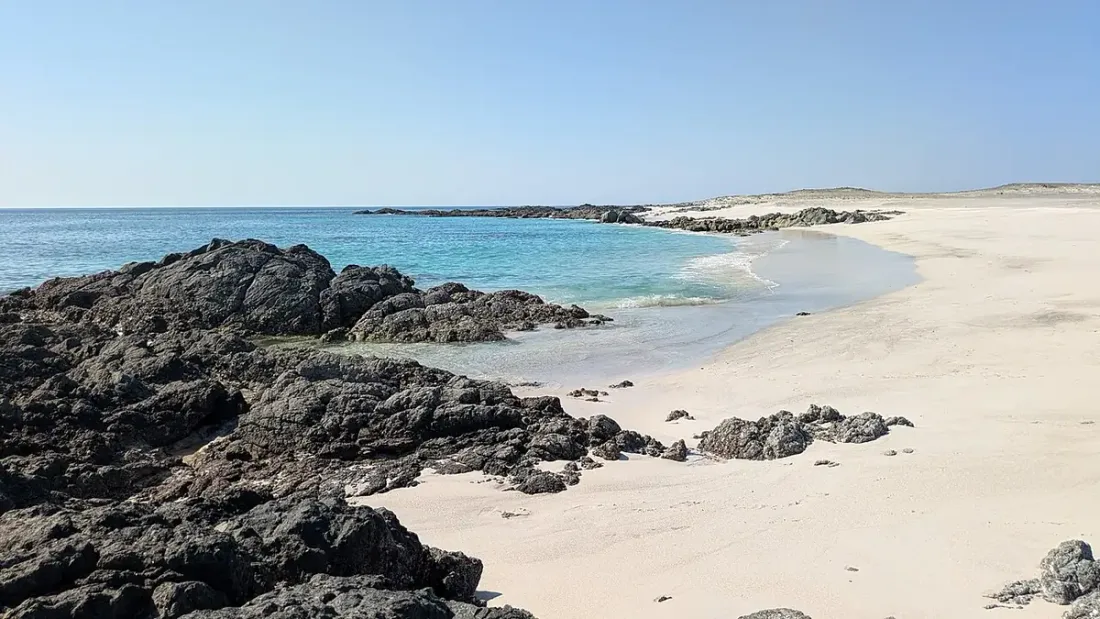 Sabbia chiara, rocce scure e acqua turchese su una spiaggia dell'isola di Masirah.