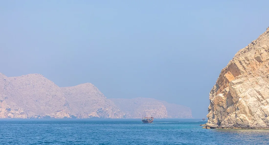 Un dhow naviga tra le alte scogliere rocciose dei fiordi del Musandam.