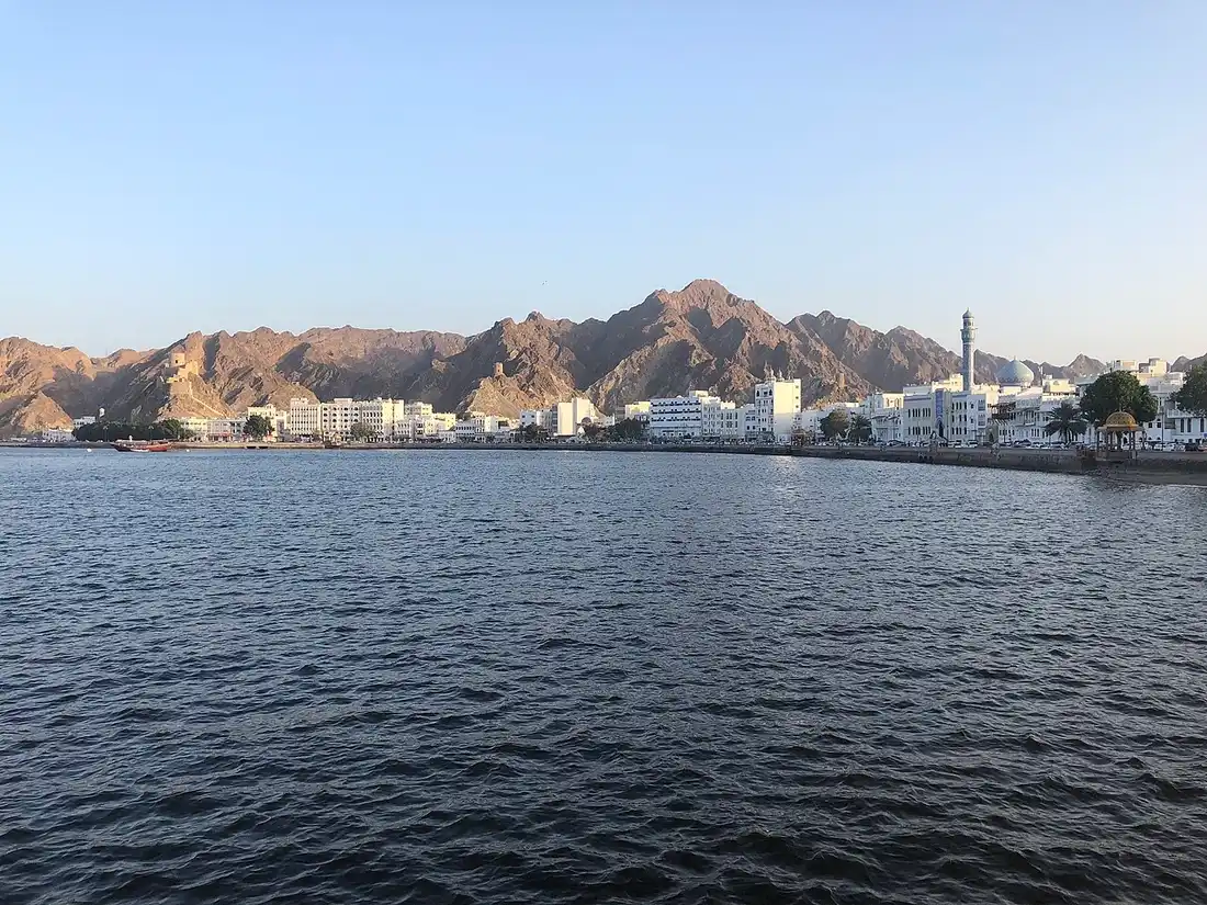 Il lungomare di Muttrah a Muscat, con edifici bianchi, minareto e montagne affacciati sul mare.