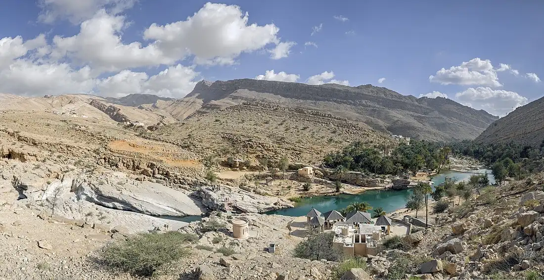 Panorama di Wadi Bani Khalid con piscine naturali, palme e montagne rocciose.